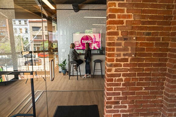 Looking through a glass office door at two women collaborating together.