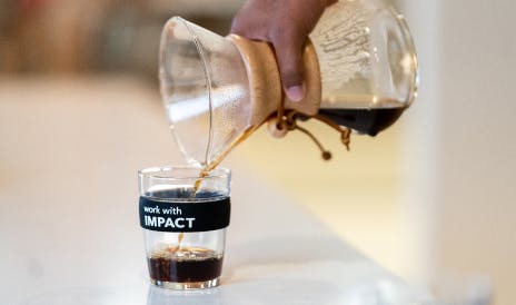 Hot coffee being poured into a 'work with impact' cup
