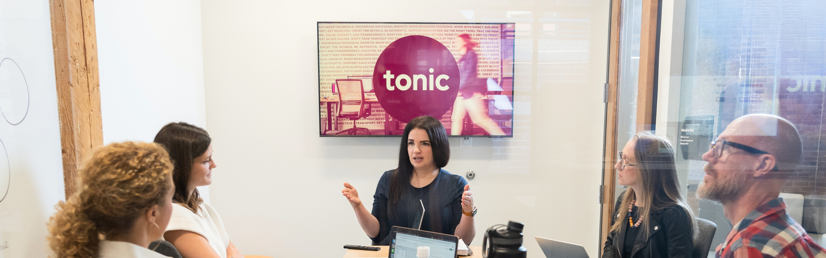 Tonic team members in a meeting discussing strategy in front of a screen displaying the Tonic logo